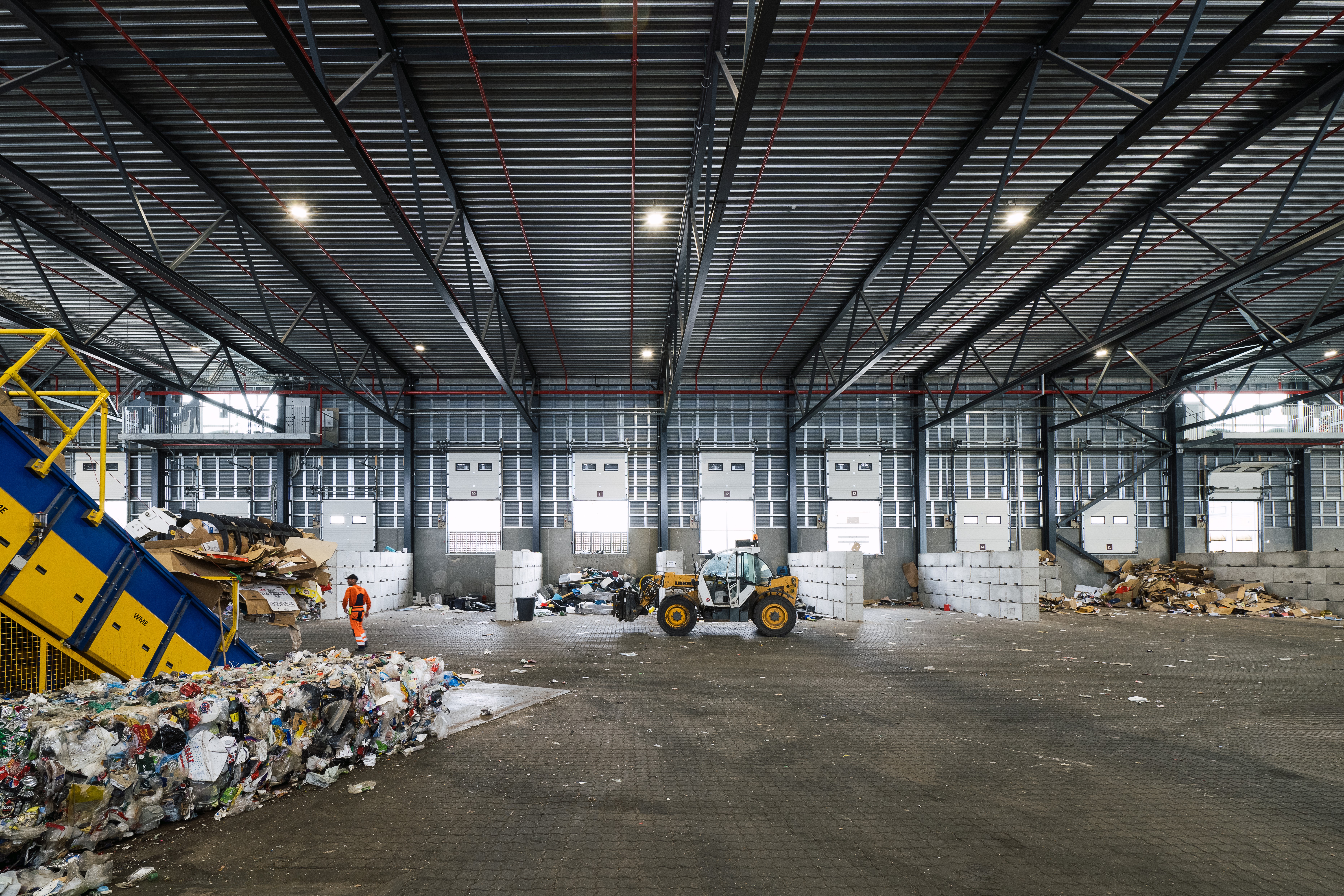 Indendørs foto af RessourceCenter Vejle's affaldssorteringshal med en gaffeltruck i arbejde og store bunker af sorteret affald, klar til videre forarbejdnin
