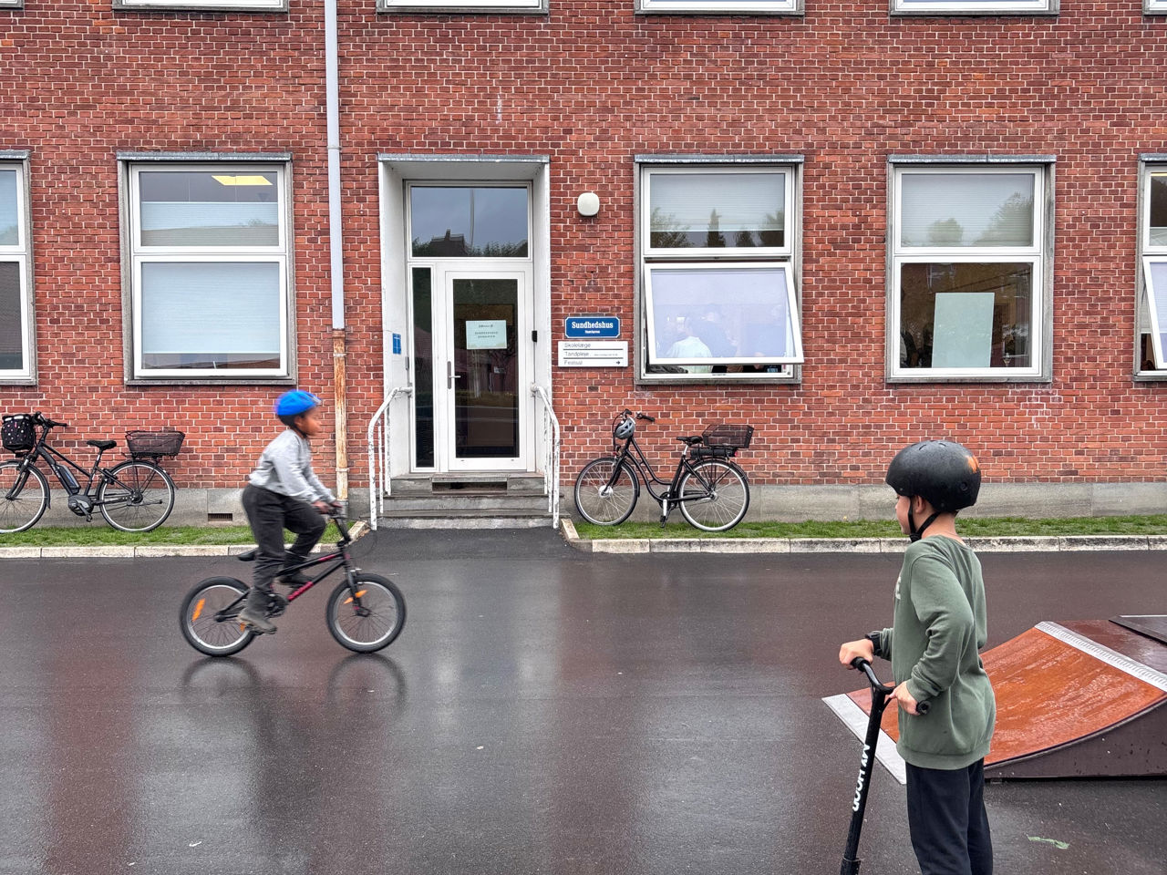 Børn cykler og kører på løbehjul foran Sundhedshus Damhaven