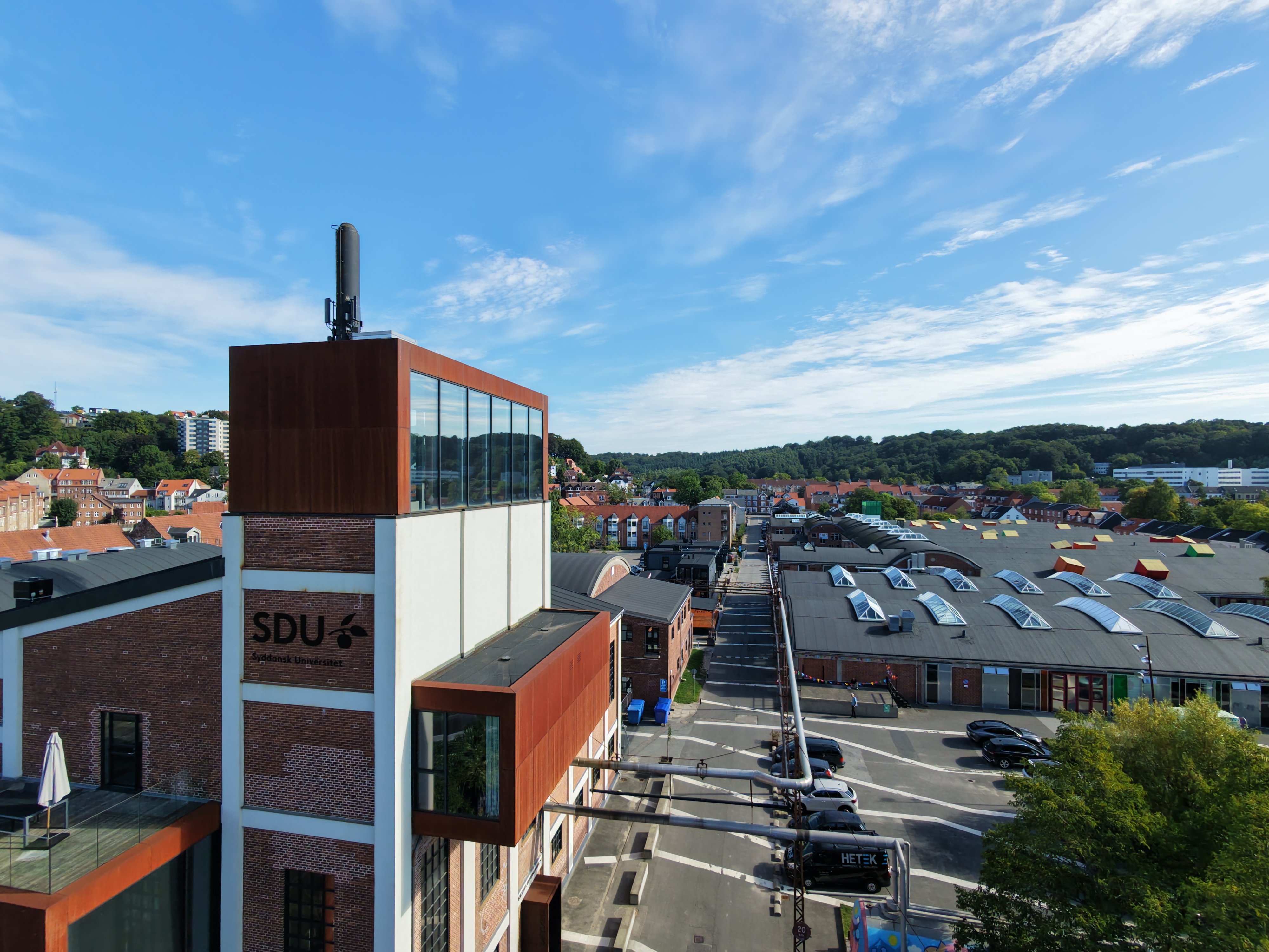 Dronebillede af Kedelbygningen med SDUs logo på siden. I baggrunden ses Spinderihallerne i Vejle.